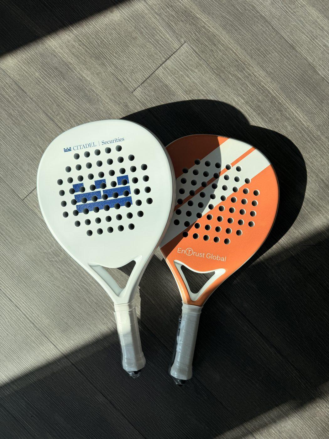 Custom-printed 'Citadel Securities' and 'EnTrust Global' padel rackets on a wood floor